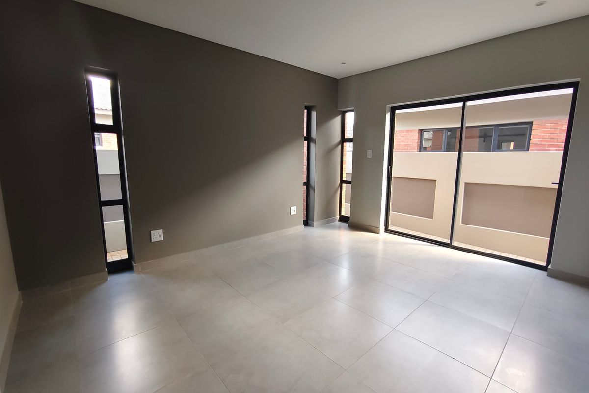 A bright, empty living room featuring large format floor tiles, modern vertical windows, and a sliding glass door leading to an outdoor area.