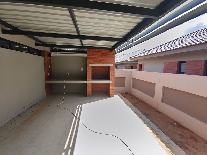 Covered patio area featuring a built-in brick braai, concrete countertop, and tiled flooring, offering a functional outdoor entertainment space.