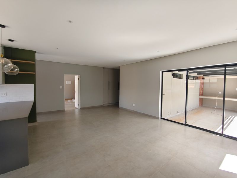 Spacious open-plan living area featuring modern tiled floors, sleek kitchen cabinetry, and large sliding glass doors leading to an outdoor patio space.