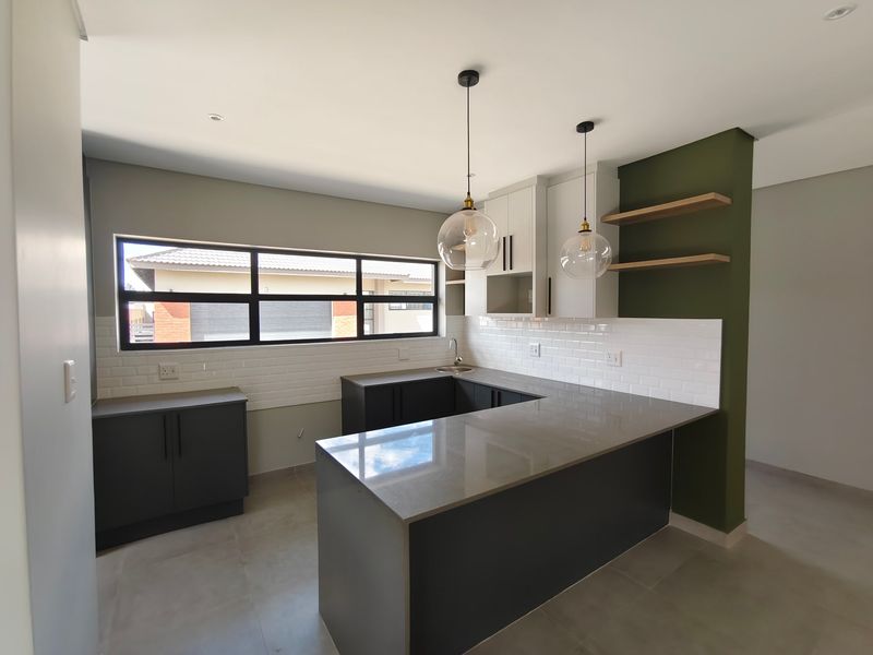 Modern kitchen featuring dark cabinetry, quartz countertops, subway tile backsplash, and floating shelves in a clean, contemporary open-plan layout.