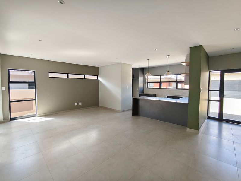 Spacious open-plan living and kitchen area featuring modern tiled flooring, neutral wall tones, and contemporary kitchen cabinetry with a central island.