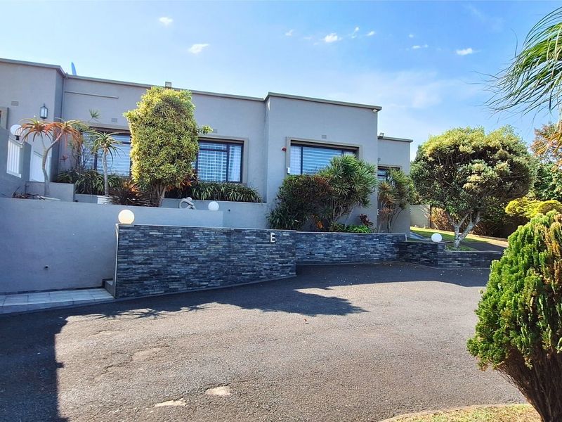 Front elevation of the property featuring a paved driveway, stone-clad retaining wall, and integrated garage access.