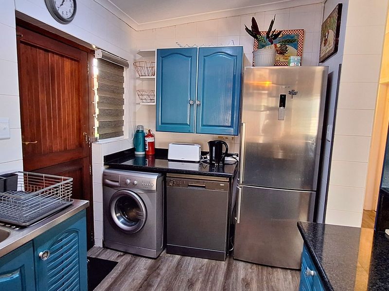 A functional kitchen featuring blue cabinetry, granite countertops, tiled backsplash, and integrated space for laundry and dishwashing appliances.