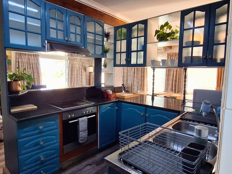 A functional kitchen featuring blue cabinetry, dark granite countertops, an integrated oven and hob, and a double sink with laminate flooring.