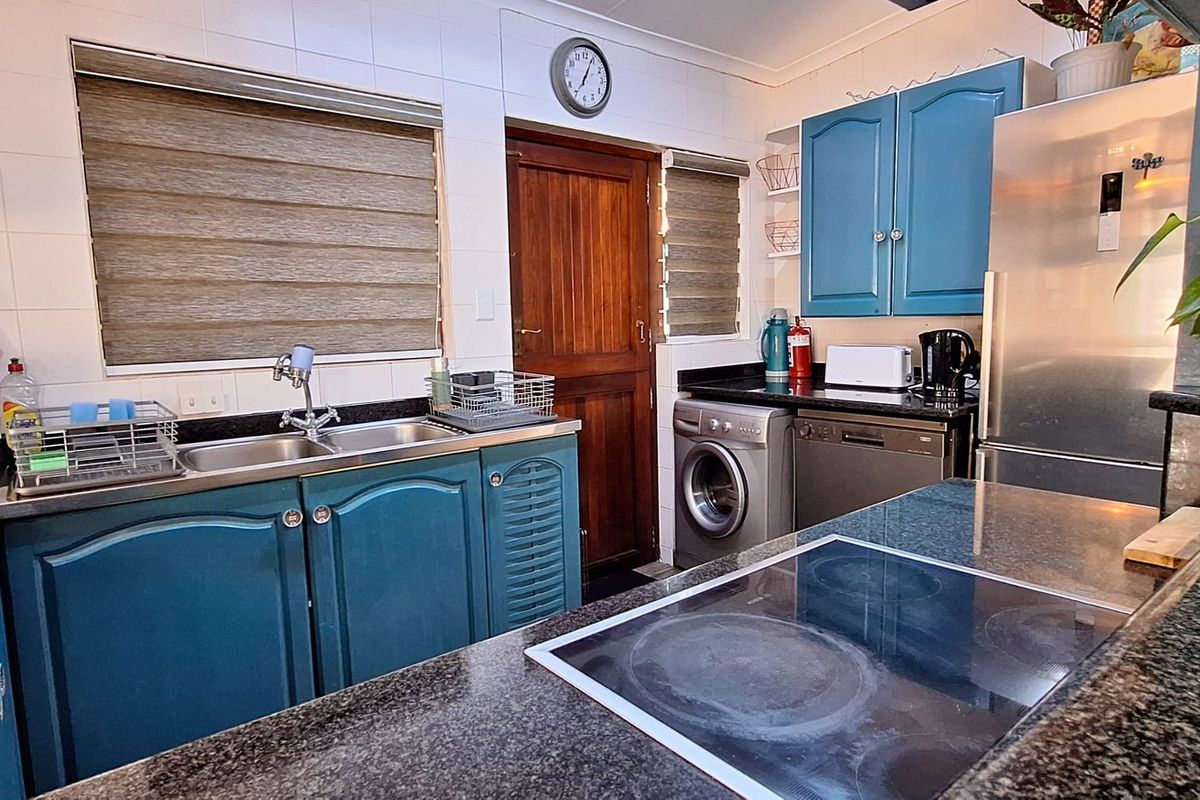 A functional kitchen featuring granite countertops, blue cabinetry, a double basin sink, and an integrated electric hob with tiled splashbacks.