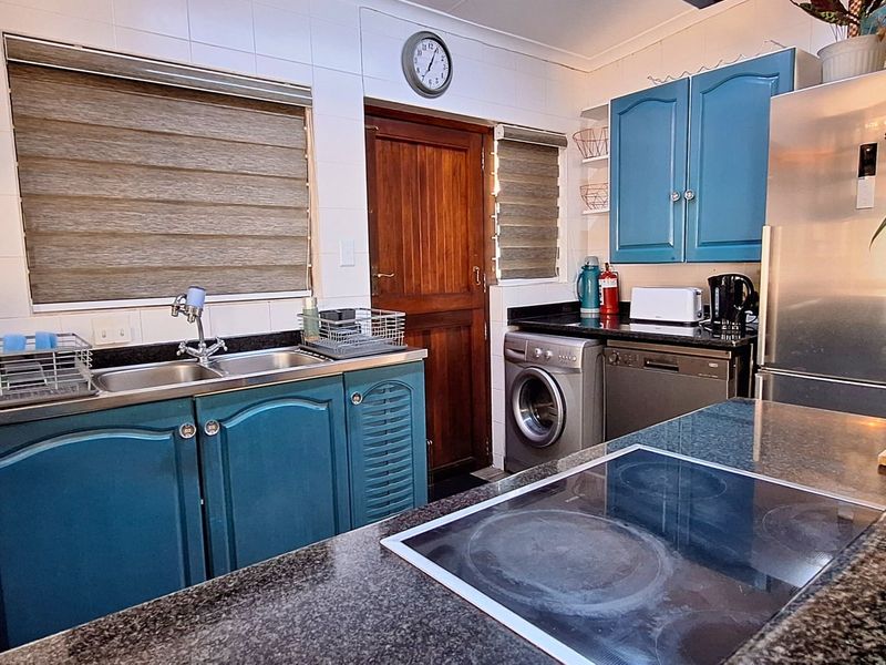 A functional kitchen featuring granite countertops, blue cabinetry, a double basin sink, and an integrated electric hob with tiled splashbacks.