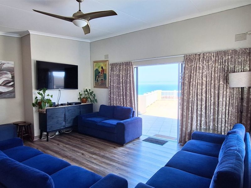Spacious living room featuring laminate flooring, a ceiling fan, and large sliding glass doors that open onto a balcony with ocean views.