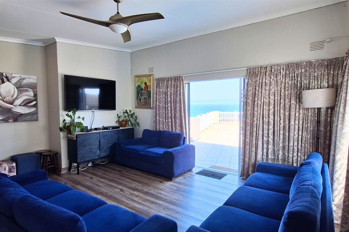 Spacious living room featuring laminate flooring, a ceiling fan, and large sliding glass doors that open onto a balcony with ocean views.