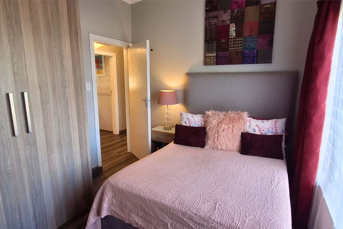 A well-maintained bedroom featuring wood-look laminate flooring and a large built-in wardrobe with modern finishes.