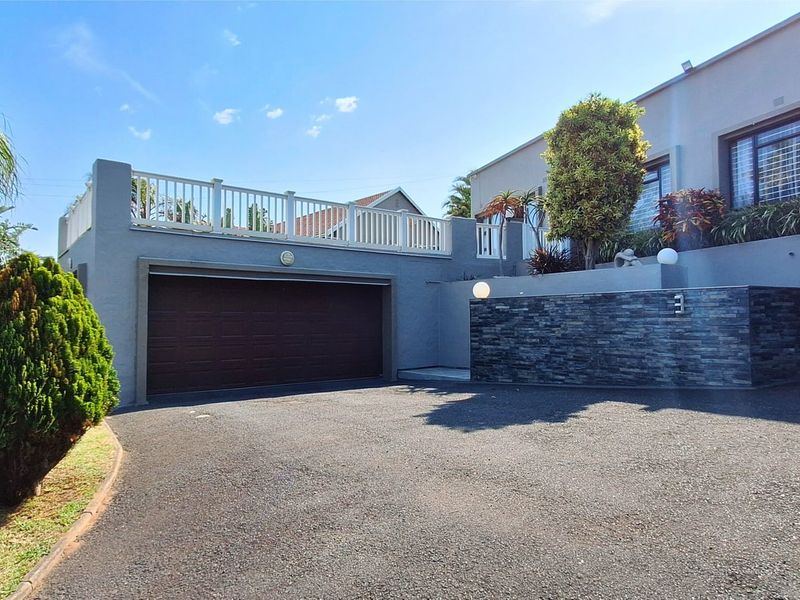 Front elevation featuring a double garage, stone-clad feature wall, and an elevated balcony with white railing, set above an asphalt driveway.
