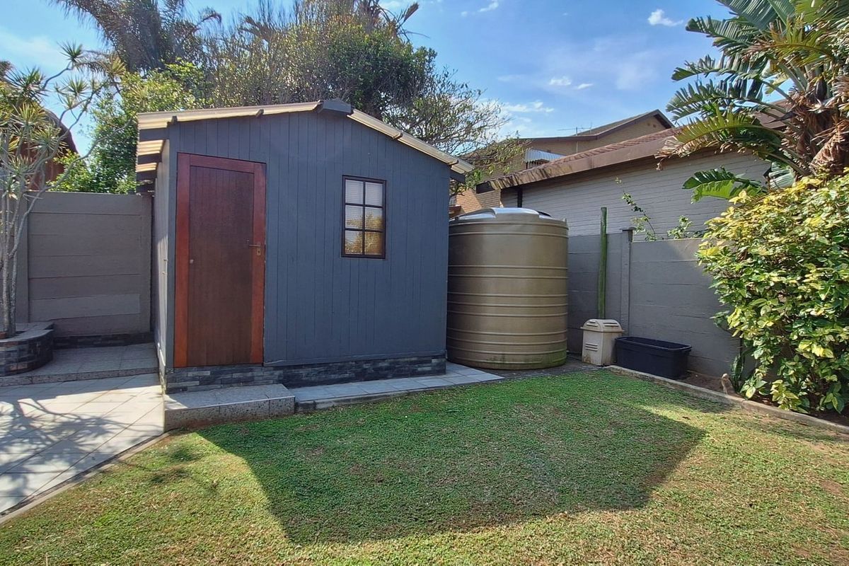A well-maintained rear garden area featuring a storage shed, a water storage tank, paved patio space, and established boundary walls.