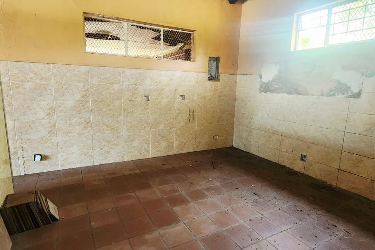 An empty kitchen space featuring tiled walls and flooring, requiring renovation and repair to restore its functionality and aesthetic appeal.