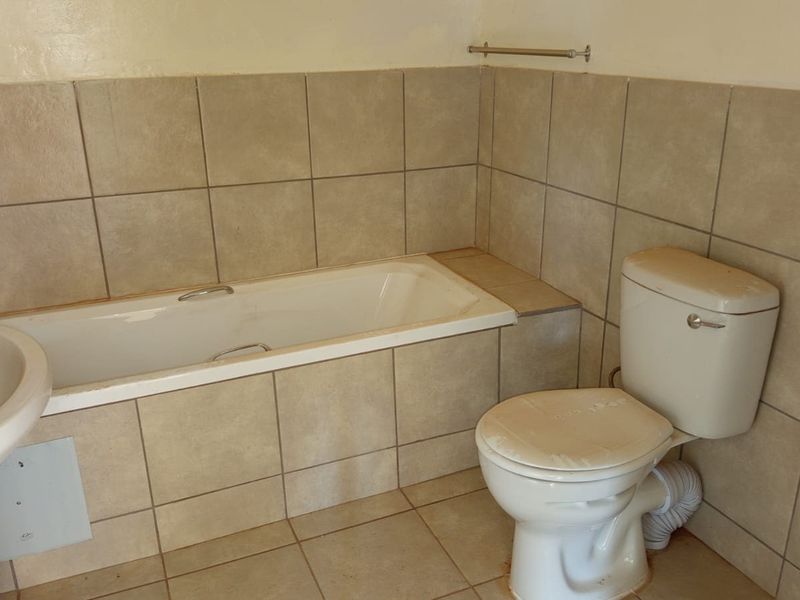 A functional bathroom featuring a built-in bathtub, pedestal basin, and toilet with neutral ceramic wall and floor tiling.