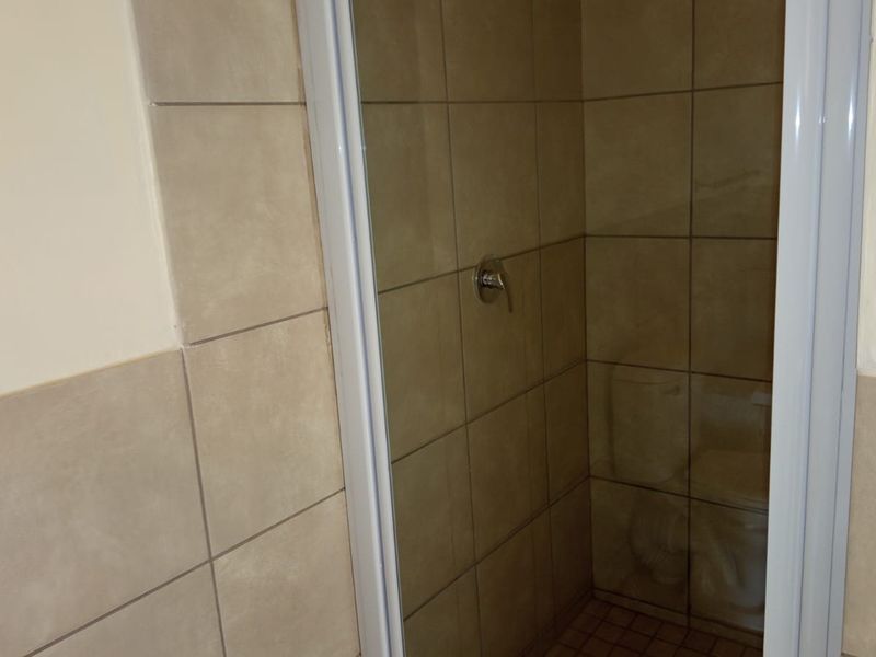 A compact bathroom shower enclosure featuring neutral wall tiles and a standard shower mixer fixture.