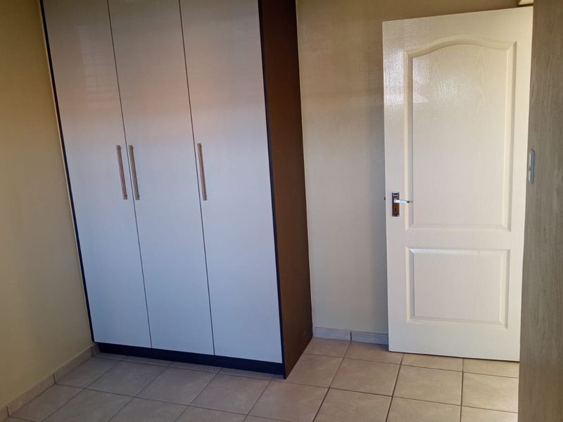 A clean, empty bedroom featuring neutral tiled flooring and a modern built-in wardrobe with white doors.