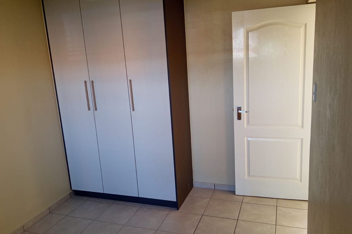A clean, empty bedroom featuring neutral tiled flooring and a modern built-in wardrobe with white doors.