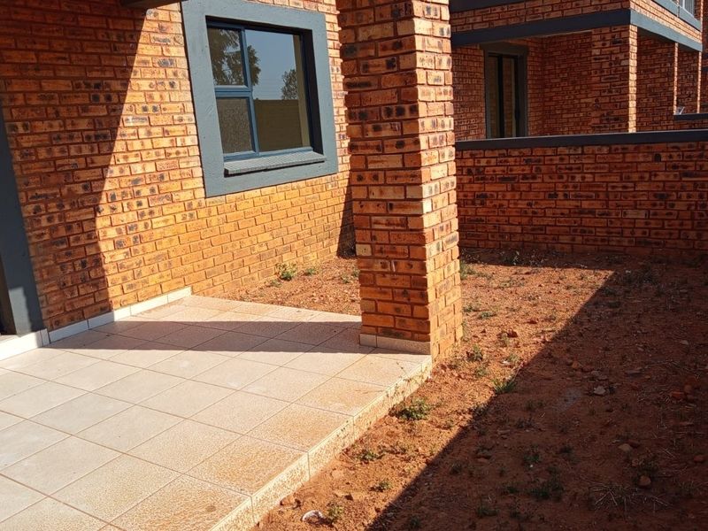 Rear exterior view of a townhouse featuring a tiled patio, face brick construction, and an unlandscaped garden area.