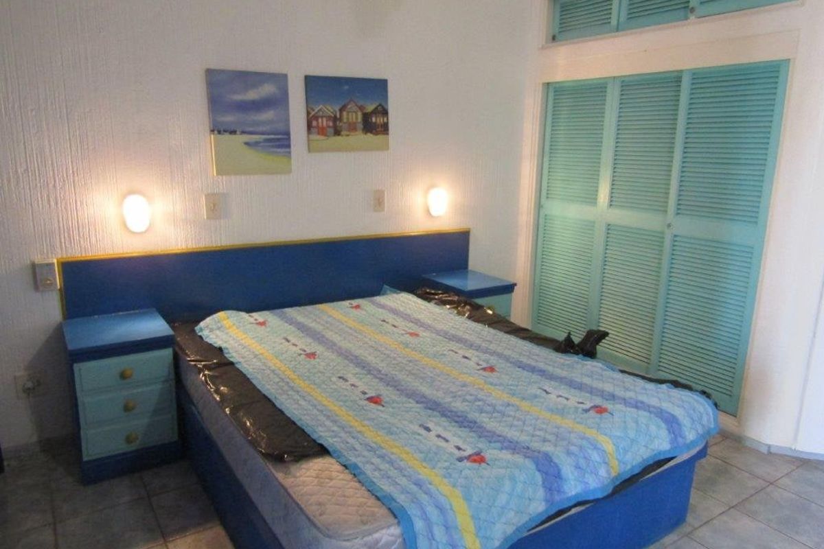 A bedroom featuring built-in cupboards with louvered doors, tiled flooring, and wall-mounted lighting. The space has a dated aesthetic and could benefit from modernization.