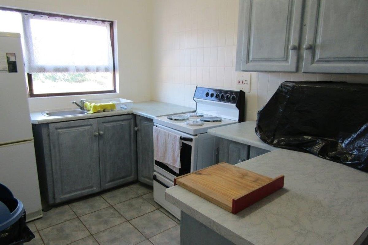 A functional kitchen featuring built-in cabinetry, laminate countertops, a stainless steel sink, and a freestanding stove with tiled backsplash and flooring.