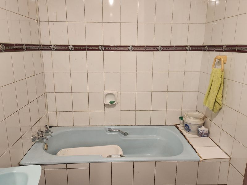 A dated bathroom featuring a built-in blue bathtub with white wall tiling and a decorative border.