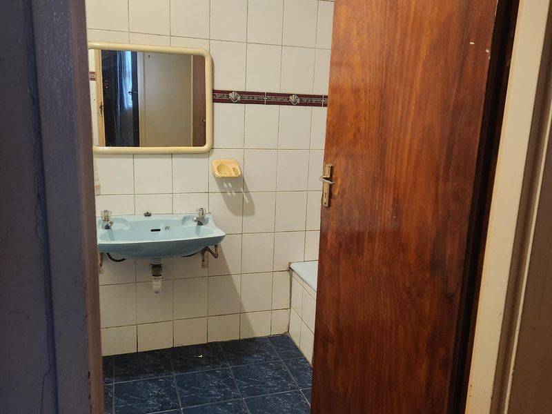 A dated bathroom featuring a wall-mounted basin, tiled walls, and a built-in bathtub, offering significant potential for a modern renovation.