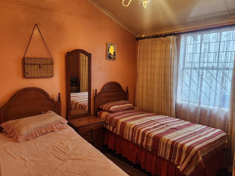 A bedroom featuring a sloped ceiling, security bars on the window, and dated wall finishes in need of maintenance.