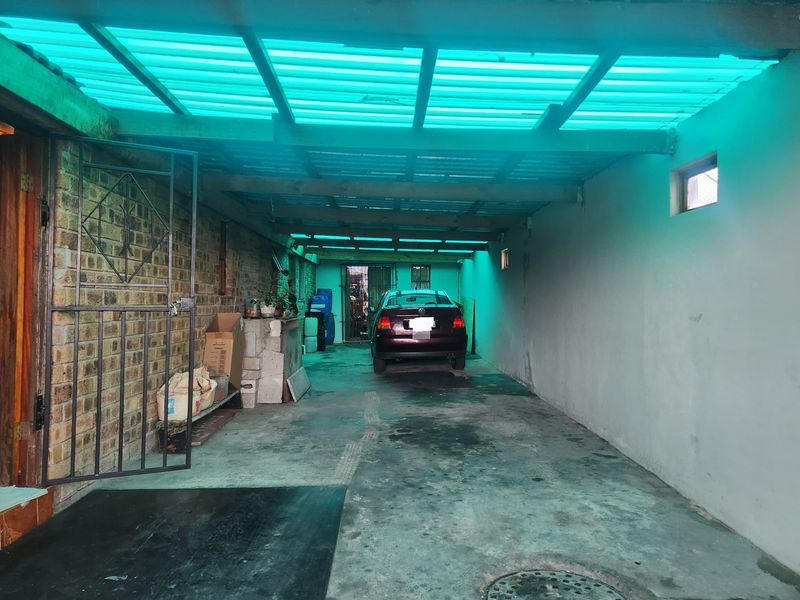 A covered garage area featuring exposed brick walls, concrete flooring, and a translucent corrugated roof structure.