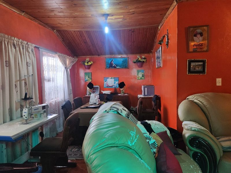 Living room featuring a vaulted timber-clad ceiling, tiled flooring, and bright orange wall finishes, offering a functional space with potential for modernization.
