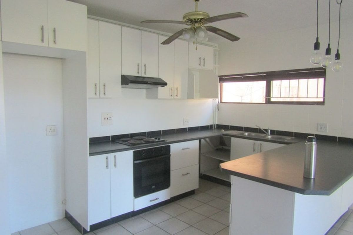 A functional kitchen featuring white cabinetry, dark laminate countertops, an integrated oven and hob, and tiled flooring.