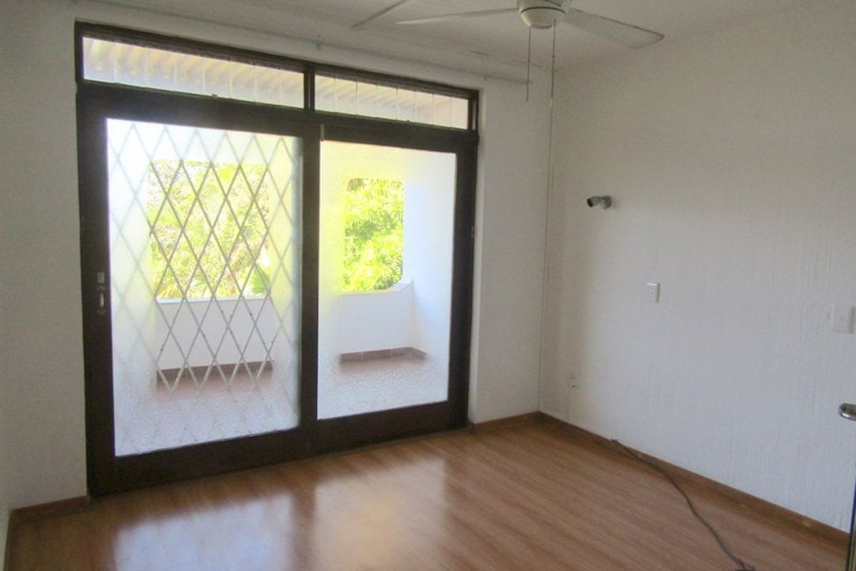 An empty bedroom featuring laminate flooring, a ceiling fan, and a large sliding glass door with a security gate leading to a balcony.