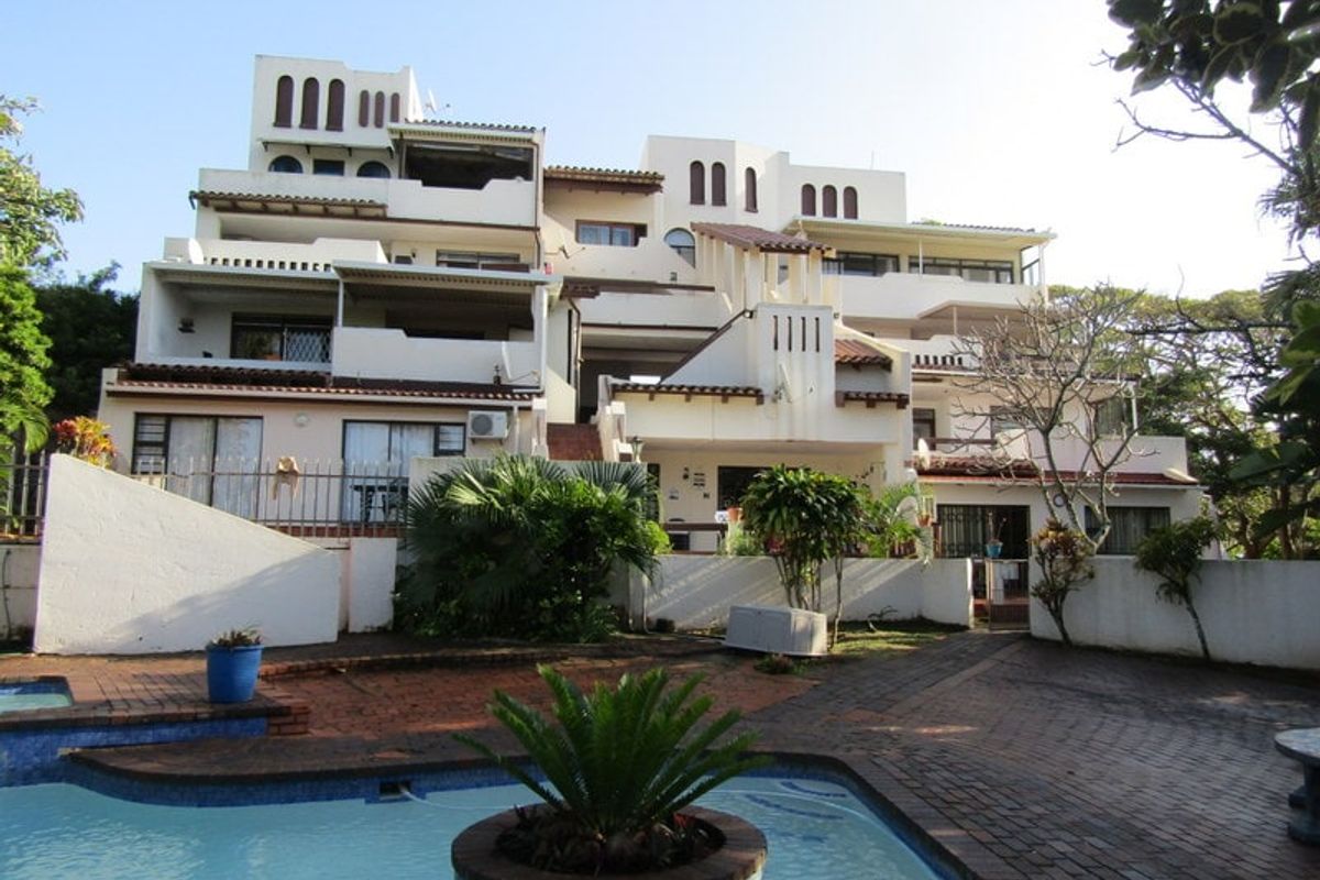 Rear view of a multi-level apartment complex featuring private balconies, a swimming pool, and paved outdoor entertainment areas.