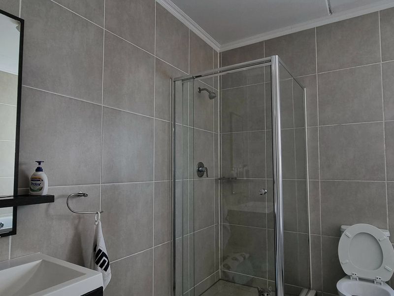 A modern bathroom featuring a glass shower enclosure, vanity basin with mirror, and neutral wall tiling.