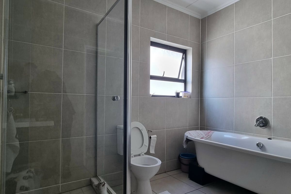Modern bathroom featuring a glass-enclosed shower, a sleek freestanding bathtub, and neutral floor-to-ceiling wall tiles.