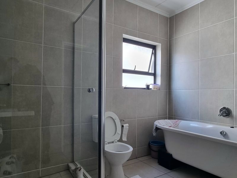 Modern bathroom featuring a glass-enclosed shower, a sleek freestanding bathtub, and neutral floor-to-ceiling wall tiles.