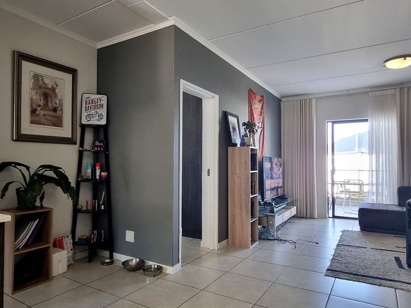 An open-plan living area featuring tiled flooring, neutral wall tones, and a sliding glass door providing access to an outdoor balcony space.