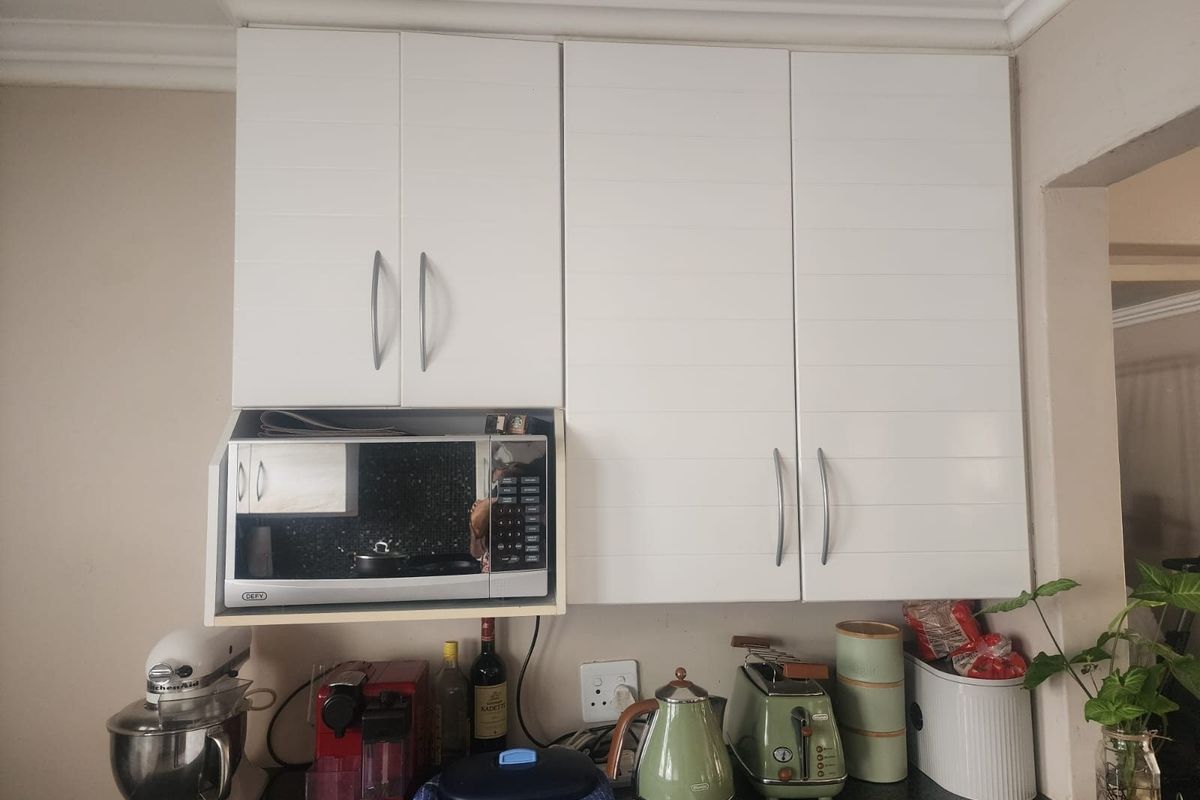 A functional kitchen area featuring white upper cabinetry with integrated microwave housing and dark laminate countertops.