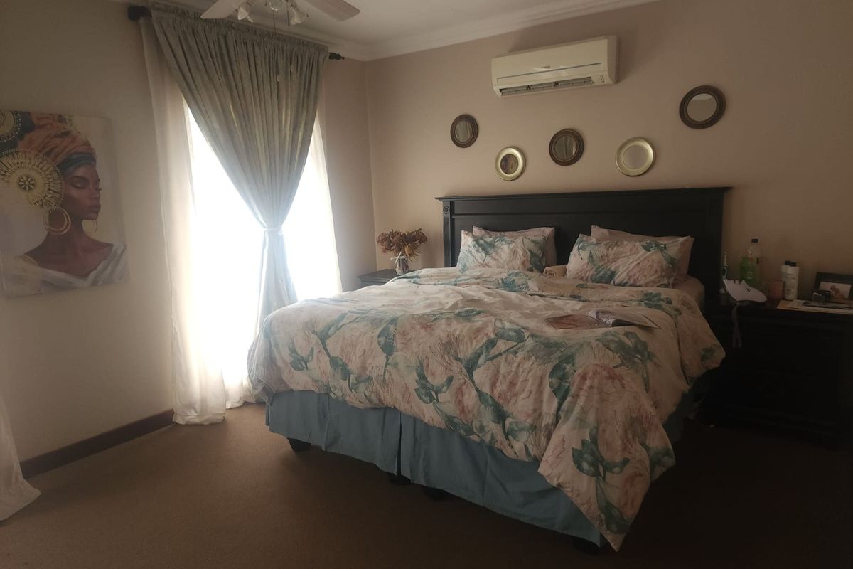 A comfortable bedroom featuring a wall-mounted split-system air conditioner, ceiling fan, and neutral carpeting.
