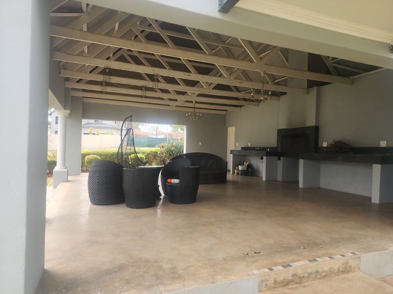 Spacious covered patio featuring exposed timber trusses, a built-in braai area with stone counters, and concrete flooring, ideal for outdoor entertaining.