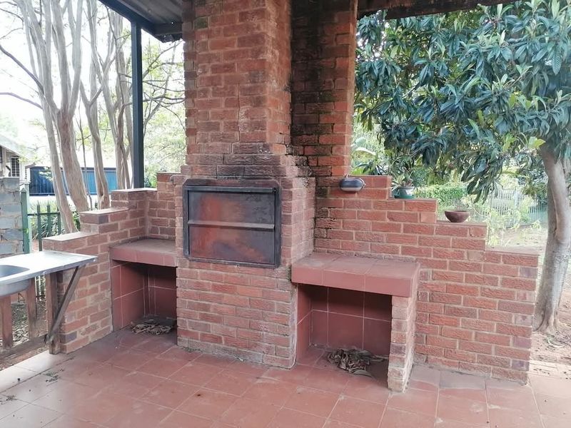Covered outdoor patio area featuring a built-in brick braai, tiled flooring, and a stainless steel prep sink, ideal for outdoor entertaining.