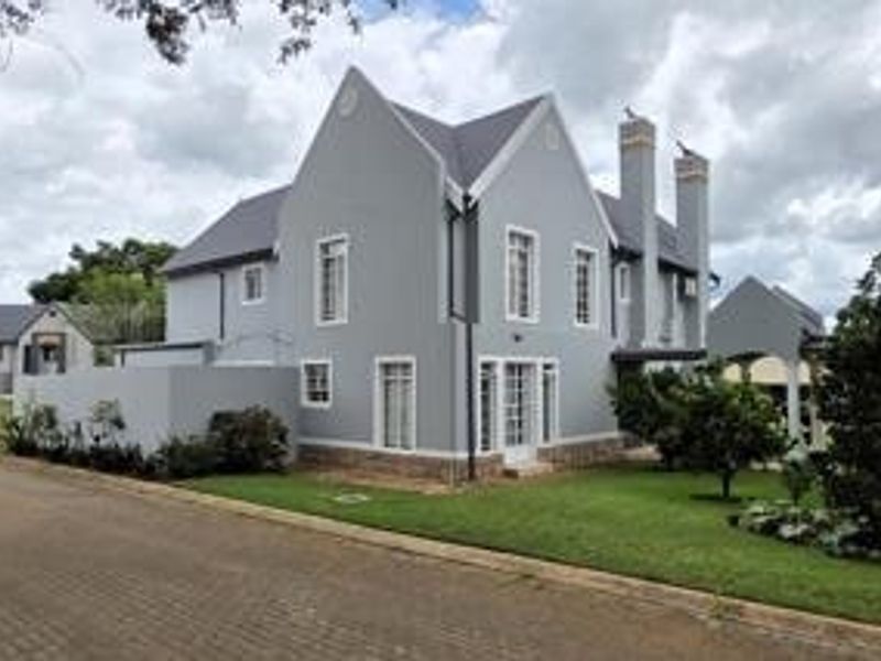 A well-maintained double-story residential property featuring a grey facade, pitched roof, chimney stacks, and a neat front lawn with a paved driveway.