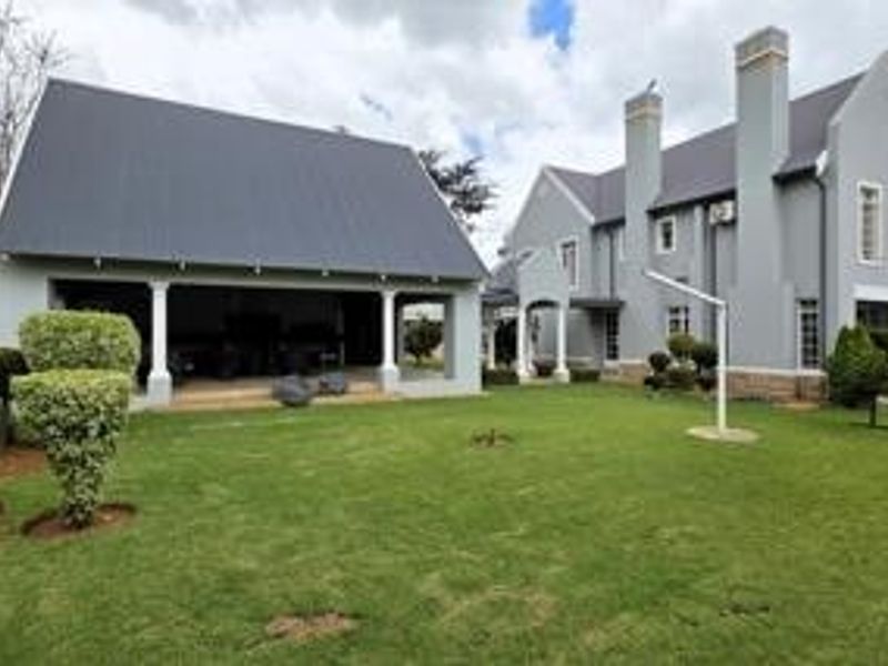 Rear view of the property featuring a large lawn, a detached garage structure with a covered patio, and the main house with prominent chimneys.