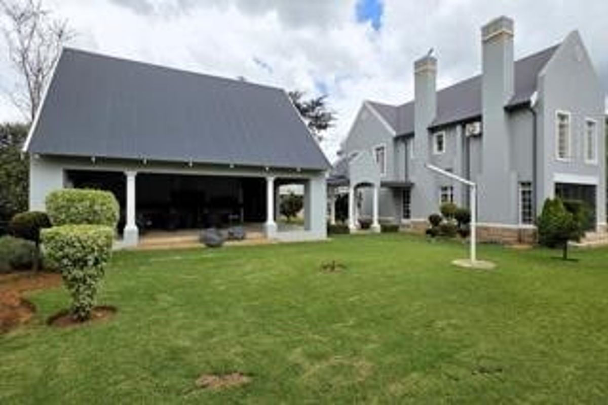 Rear view of the property featuring a large lawn, a detached garage structure with a covered patio, and the main house with prominent chimneys.