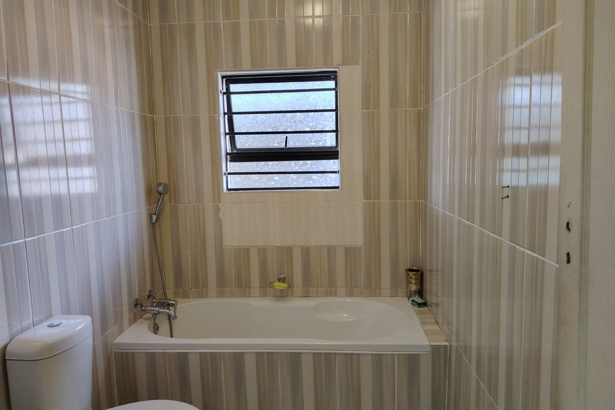 A functional bathroom featuring a built-in bathtub with a handheld shower mixer, a toilet, and floor-to-ceiling striped ceramic wall tiles.