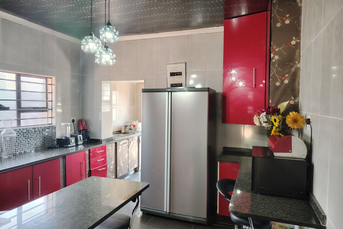 A functional kitchen featuring red cabinetry, granite countertops, a breakfast bar, and a dedicated scullery area for additional prep and storage.