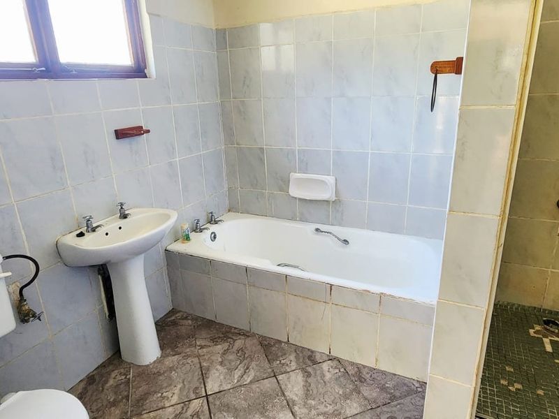 A dated bathroom featuring a pedestal basin, built-in bathtub, and separate shower enclosure with tiled finishes throughout.