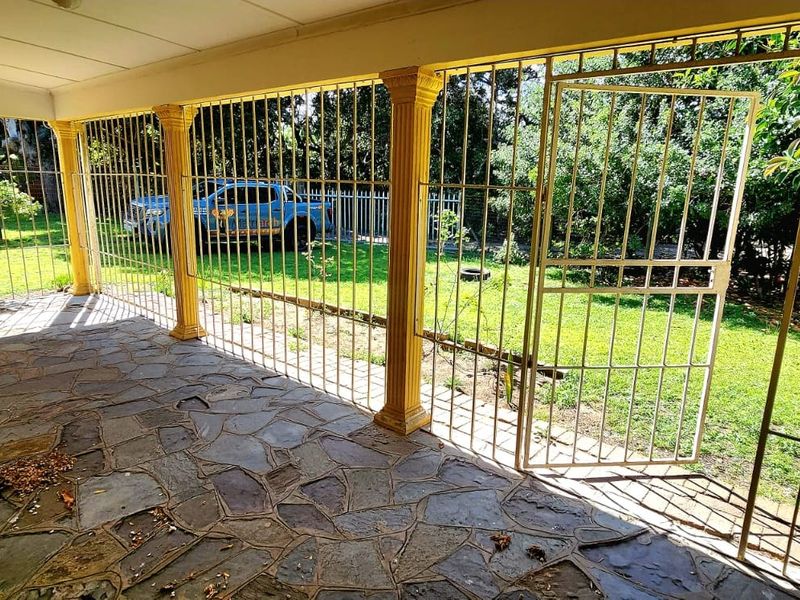 A covered patio area featuring stone flooring, decorative columns, and full-length security bars overlooking the garden.