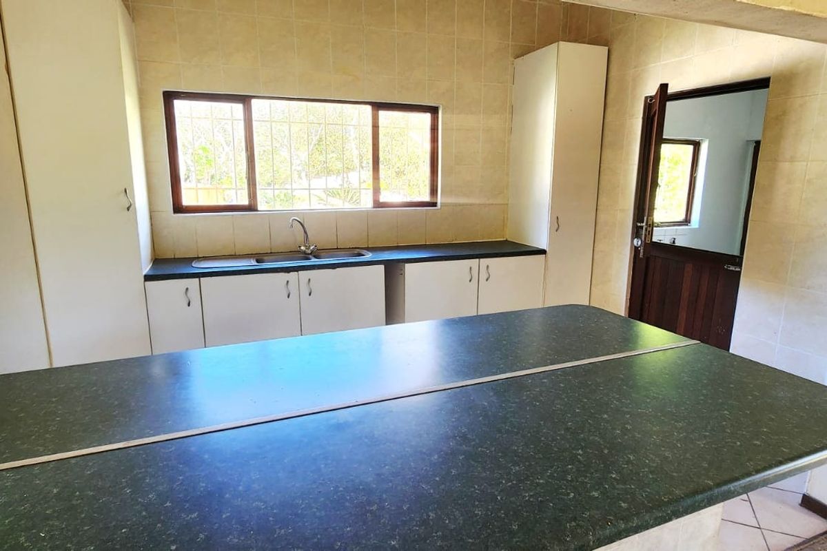 A functional kitchen featuring built-in cabinetry, laminate countertops, and a double basin sink, framed by a classic architectural archway.