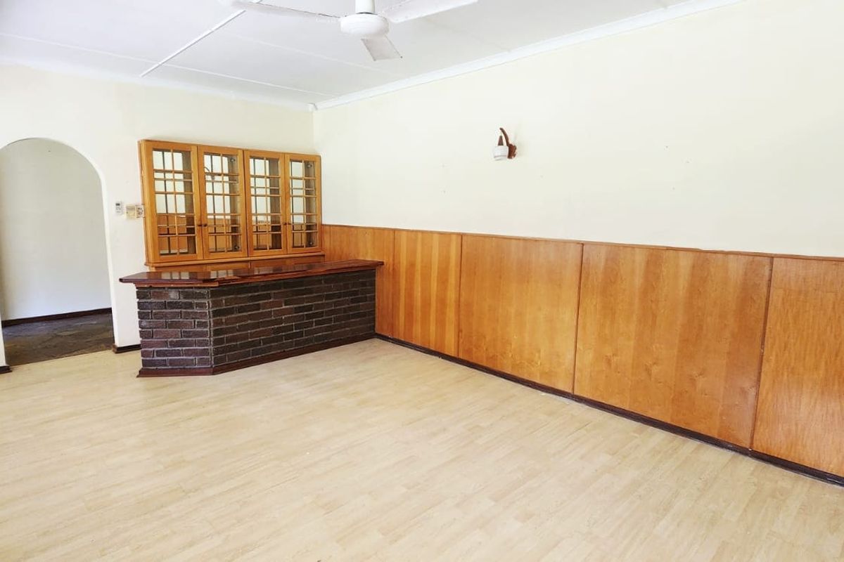 Spacious living area featuring a built-in brick bar, timber wall paneling, and a ceiling fan, offering a versatile layout for renovation.