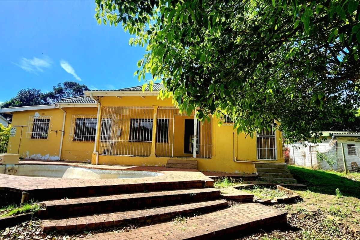 Rear view of a yellow house featuring a swimming pool, brick patio area, and security bars on windows, set within a garden.