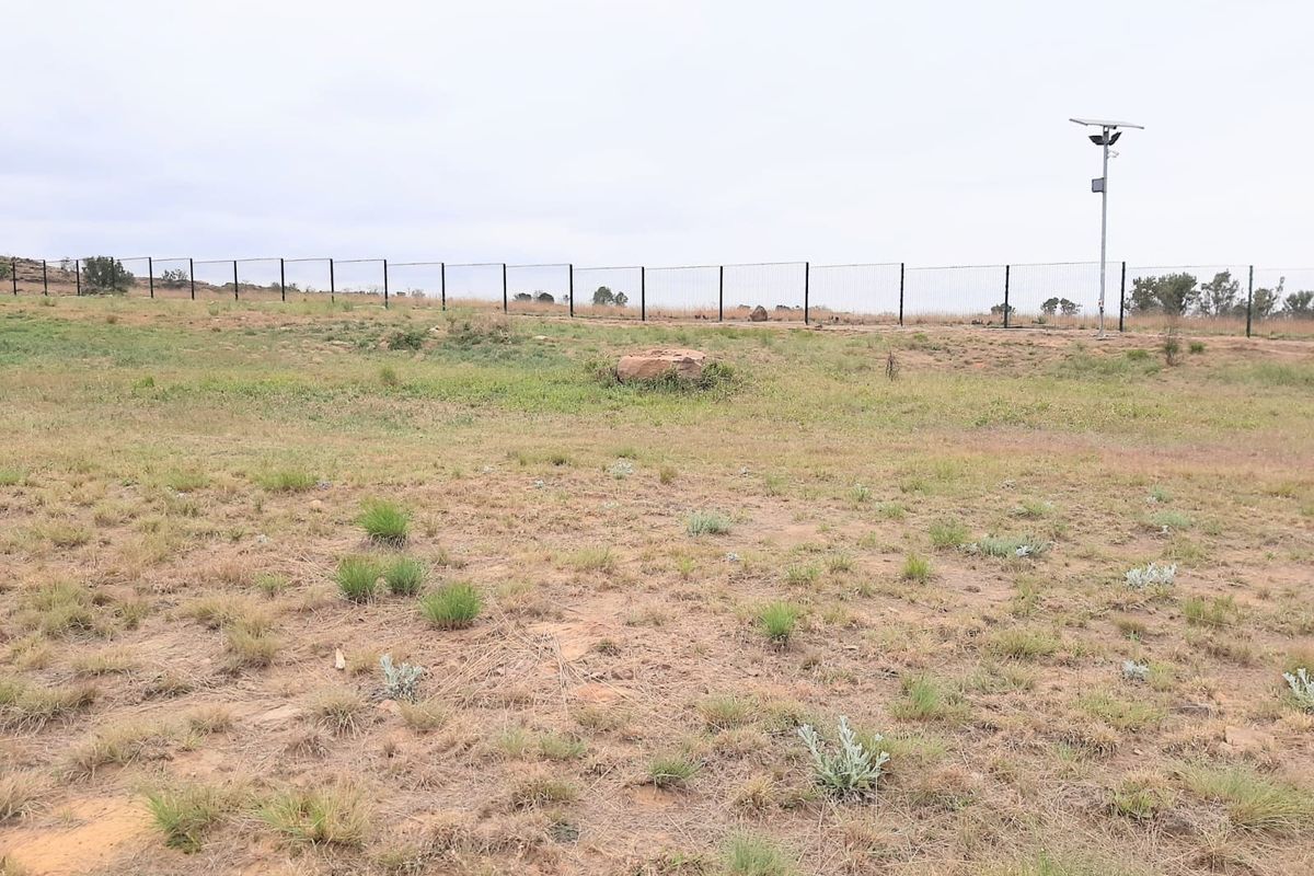 A vacant residential plot featuring natural grass terrain, perimeter fencing, and a solar-powered security light pole.